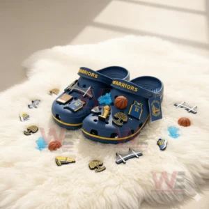 Alt text: A close-up of a pair of blue Crocs decorated with Golden State Warriors-themed charms on a fluffy white rug.