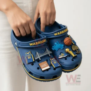 Alt text: A person holding a pair of Golden State Warriors Crocs decorated with themed charms.
