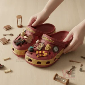A pair of red and gold clogs featuring multiple themed charms placed on a wooden surface with small decorative items around.
