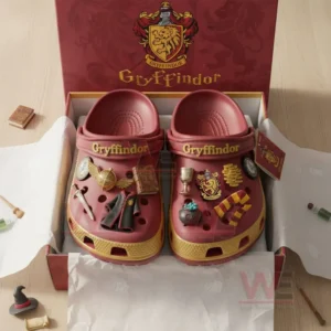 Griffindor Premium Crocs Crocband Clogs With Charms 5 A boxed pair of red and gold clogs featuring multiple themed charms with small props around on a wooden table.