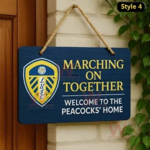 Home of Football Hanging Welcome Sign 9 A blue wooden hanging sign with the Leeds United crest and motto displayed next to a wooden door on a brick wall.