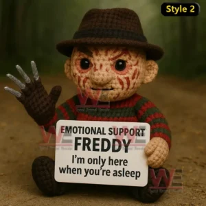 A crochet doll with a brown hat and striped sweater sitting on a forest path holding a sign with a humorous message about sleep!
