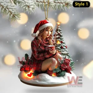 A decorative ornament of a girl in red sitting on snow beside a lit holiday tree.