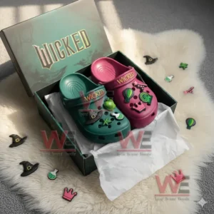 A box of Wicked themed Crocs with one green and one pink shoe decorated with charms like a witch hat and crown on white tissue paper.