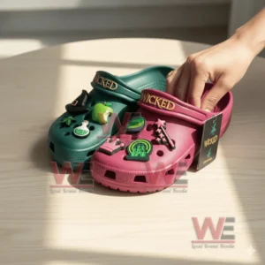 A close view of Wicked Crocs on a wooden table with a hand touching the pink shoe showing various themed charms.