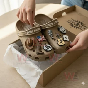 Jason Aldean Crocs Crocband Clogs With Charms 8 Hands holding brown clogs with country themed charms above a box.