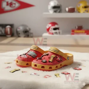 Red Crocs with Kansas City Chiefs-themed charms on display with football helmets and memorabilia in the background.