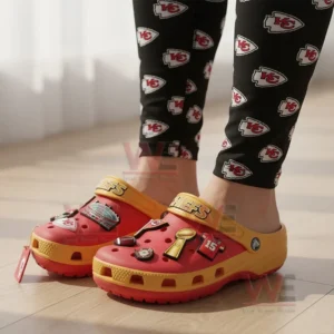 A person wearing Kansas City Chiefs-themed Crocs and leggings with the team logo in a bright indoor setting.