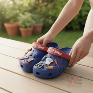 Kansas City Royals Crocs Crocband Clogs With Charms 7 A person holding blue Kansas City Royals Crocs decorated with baseball charms in a sunny outdoor setting.