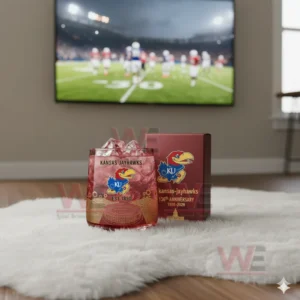 Kansas Jayhawks whiskey glass filled with red drink and ice, sitting on the floor with a football game on the TV in the background.