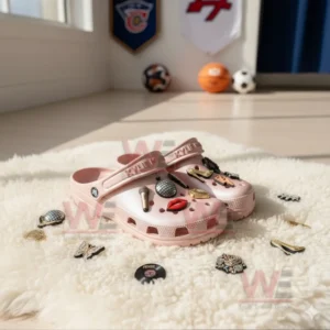 Pink Kylie Minogue-themed Crocs with various charms displayed on a rug with sports memorabilia in the background.
