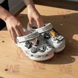 Close up of hands adjusting gray Las Vegas Raiders Crocs adorned with detailed team themed decorations on a light wooden background!