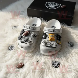 Gray Crocs with Las Vegas Raiders logo and sports themed charms displayed near black Raiders box on soft carpet!
