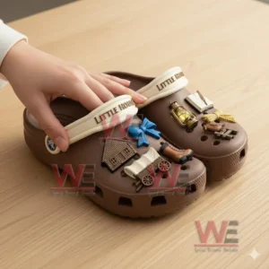 Brown clogs with various themed charms being handled on a wooden table!