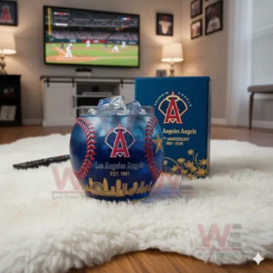 Los Angeles Angels whiskey glass with blue drink and ice, sitting on a rug with a baseball game on the TV in the background.