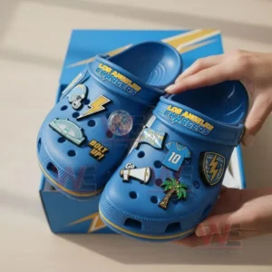 A person wearing Los Angeles Chargers Crocs with football and team-related charms in a bright indoor setting.
