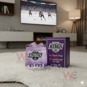 A Los Angeles Kings anniversary whiskey glass with ice on a white rug in front of a television showing a hockey game.