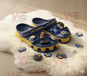 Blue and yellow Crocs with Los Angeles Rams logo and sports themed charms displayed on white rug under warm light!