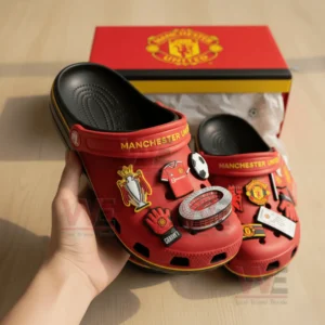 Red Manchester United Crocs decorated with football-related charms inside a team-branded box.