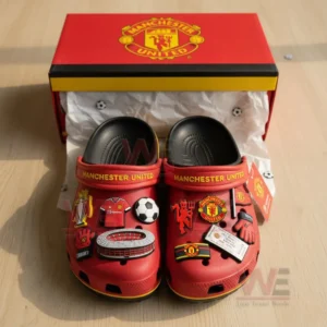 A person holding red Manchester United Crocs with football-themed charms attached to them.