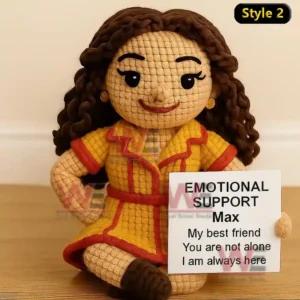 Max and Caroline Emotional Support Doll 4 A crochet doll with brown hair and a yellow outfit holding an emotional support sign while sitting on a floor!