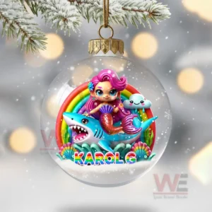 A clear ornament showing a mermaid riding a shark with a rainbow behind in a snowy scene!