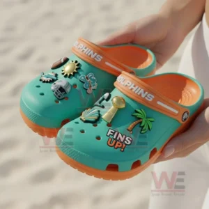 Miami Dolphins Crocs Crocband Clogs With Charms 8 Alt text: Person holding Miami Dolphins-themed Crocs with NFL-themed charms in a beach setting.
