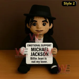 Michael Jackson Emotional Support Doll 5 A crochet doll with a black hat and suit sitting on a table holding a message sign!