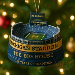 Christmas ornament resembling Michigan Stadium with blue and gold design hanging on a tree.