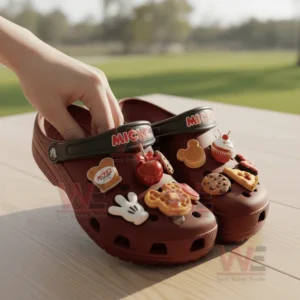 Red clogs with assorted themed charms held by a hand on a wooden outdoor surface!
