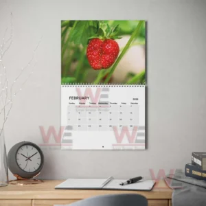 A calendar page with a strawberry photo above the dates for February two thousand twenty six hanging on a wall near a desk!