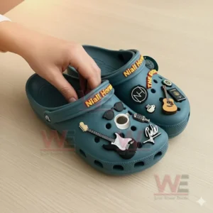 Hand holding teal Niall Horan Crocs with musical charms on a wooden surface!