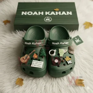 Green Noah Kahan themed Crocs with nature and music related charms displayed in a matching box on white fur!