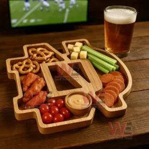 An emblem shaped wooden tray filled with assorted snacks sits on a wooden table next to a glass of beer with a sports screen in the background!