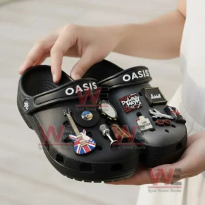Oasis Crocs with Charms 8 A person holding black Oasis Crocs decorated with rock themed charms and the band’s logo on the straps.