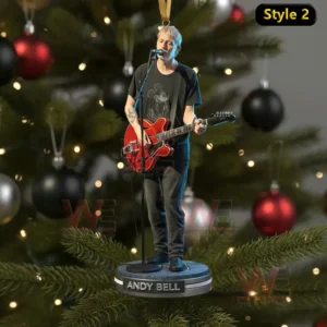 A guitarist figure with a red instrument hangs as an ornament on a Christmas tree decorated with dark and metallic ornaments.
