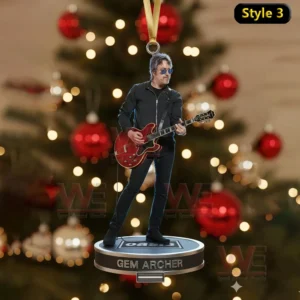 A musician with sunglasses and a red guitar stands on a round ornament hanging from a Christmas tree decorated with red and gold lights.