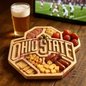 A wooden platter with an Ohio State design surrounded by assorted snacks sits near a glass of beer with a sports game on a television!