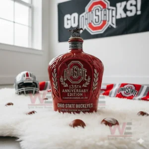 A red Ohio State anniversary bottle is positioned on a white rug with a banner a helmet and buckeye nuts nearby!