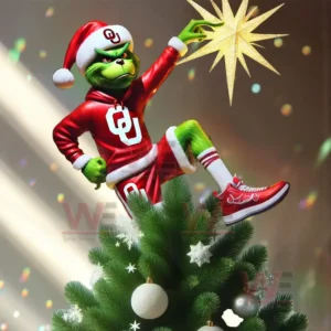 A green figure in Oklahoma Sooners Santa clothes standing on a Christmas tree placing a bright golden star on top!