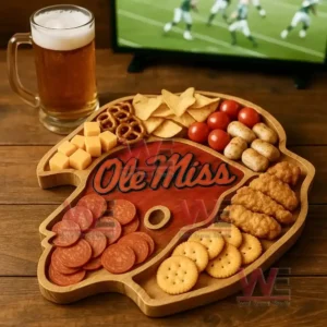 A wooden platter with an Ole Miss design surrounded by assorted snacks sits near a glass of beer with a sports game on a television!