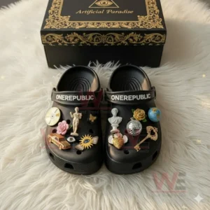 Black OneRepublic Crocs with artistic charms placed before a gold patterned box on a white fur background!
