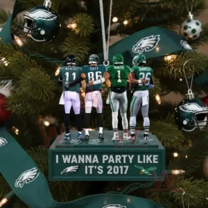 Four football players in green uniforms stand arm in arm on a square ornament hanging from a Christmas tree decorated with green ribbons and helmet ornaments.