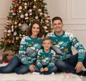 Alt text: A family of three wearing Miami Dolphins-themed Christmas sweaters sitting on the floor with a Christmas tree in the background.