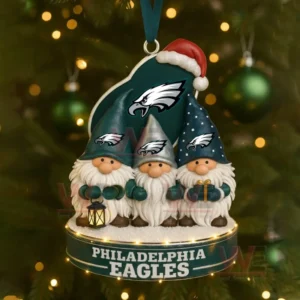 Three gnome figures in green themed outfits stand on a round ornament hanging from a Christmas tree decorated with green lights and baubles.