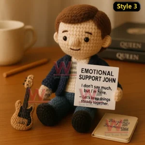 Queen Band Emotional Support Doll 9 A crochet doll with short brown hair sitting near a mini bass guitar holding an emotional support message sign!