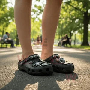 Close-up of a person’s feet wearing black Queensryche clogs with band-themed decorations while standing on a park road.