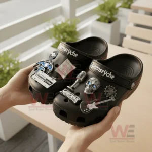 Hands hold a pair of black Queensryche clogs decorated with band-related charms and emblems in a bright outdoor setting.