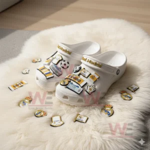 White Real Madrid decorated clogs resting on a white fluffy mat with various charms scattered around.