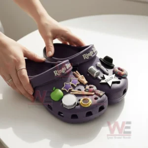 Hands holding purple Ringo Starr clogs decorated with music themed charms.